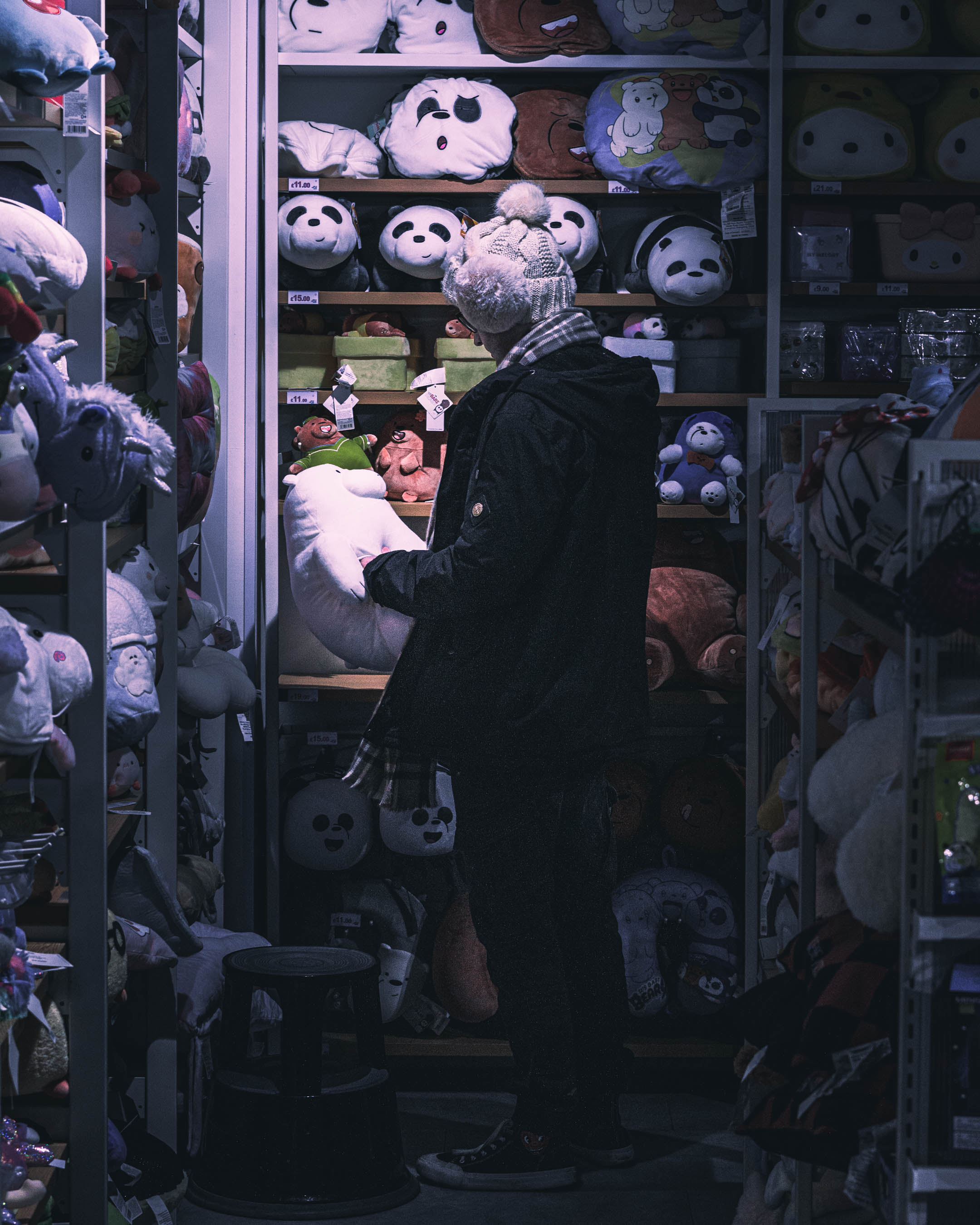 Photograph of a man standing in the corner of a Miniso store clutching a white bear.