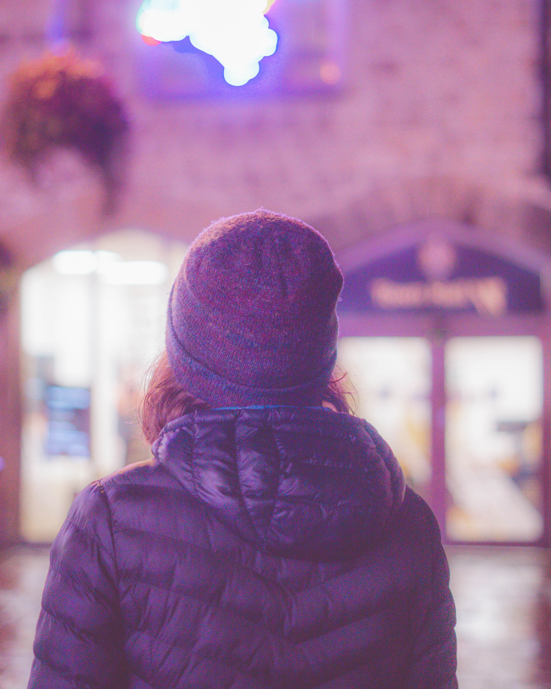 Photograph of a woman's top half from behind, blurred light display at top of background.